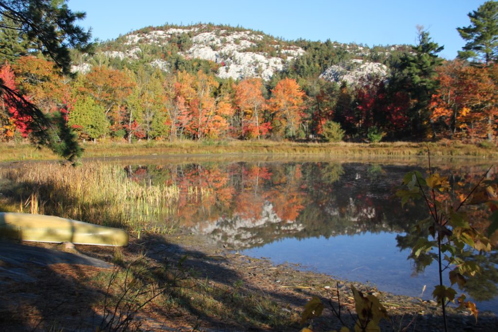 canoe by a lake below a colourful fall mountain