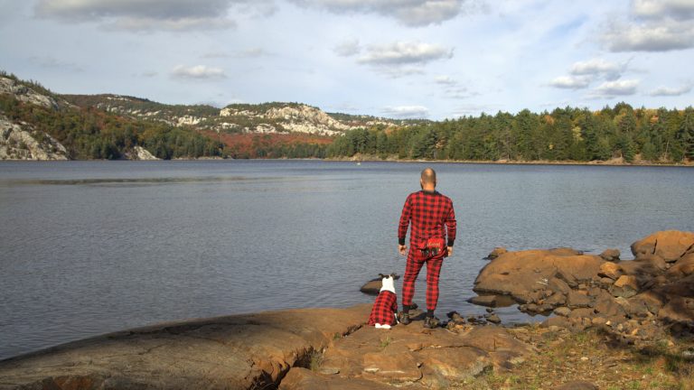 A man and a dog wearing matching pajamas look out onto a lake and mountains