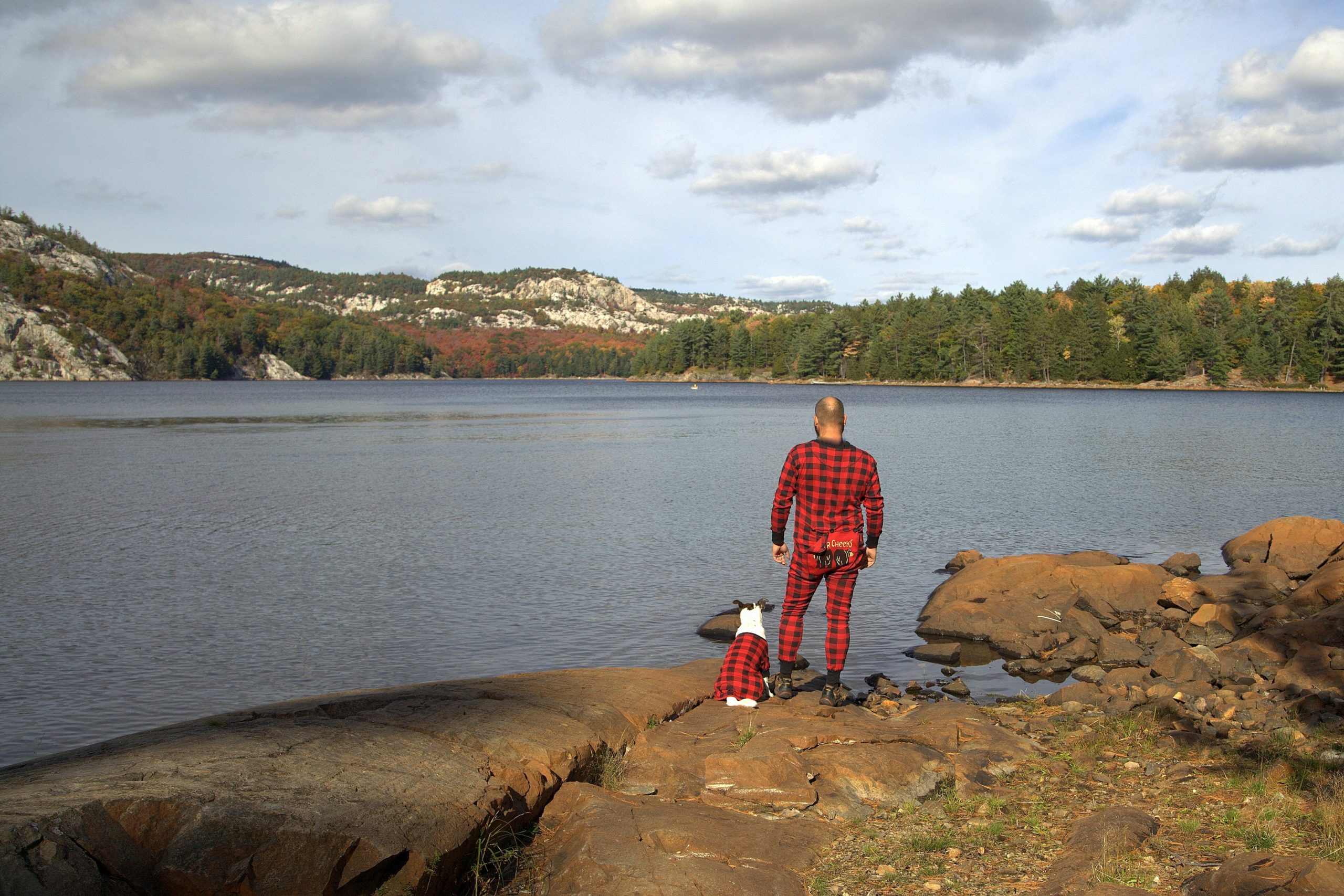 A man and a dog wearing matching pajamas look out onto a lake and mountains