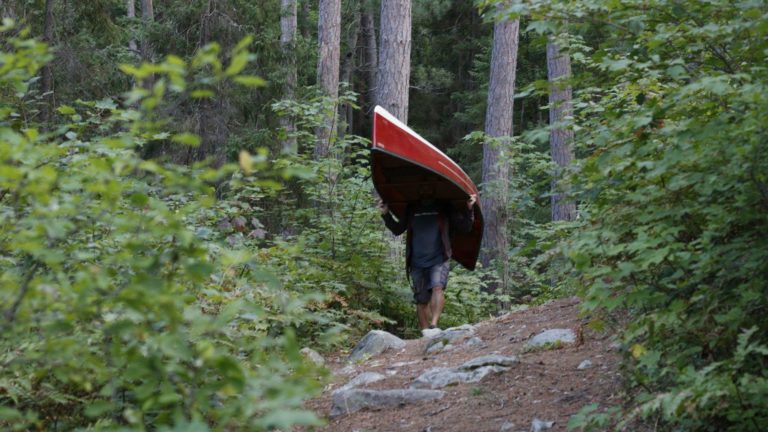 man portaging a red canoe