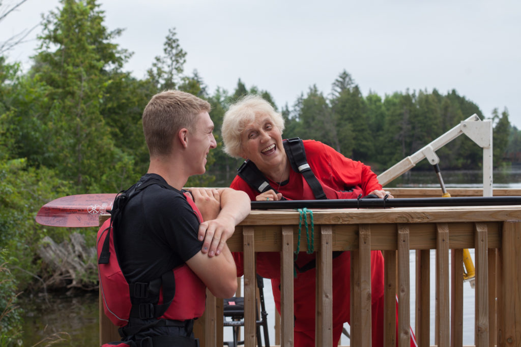 A lady jokes with a volunteer, both wearing PFDs