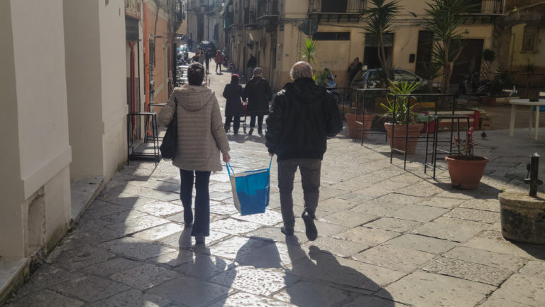 old couple walk down a street holding the same bag