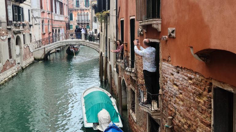 Husband takes a photo from a window over a canal of his wife in another window, Venice, Italy